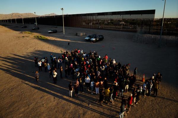 a group of migrants by the border wall 